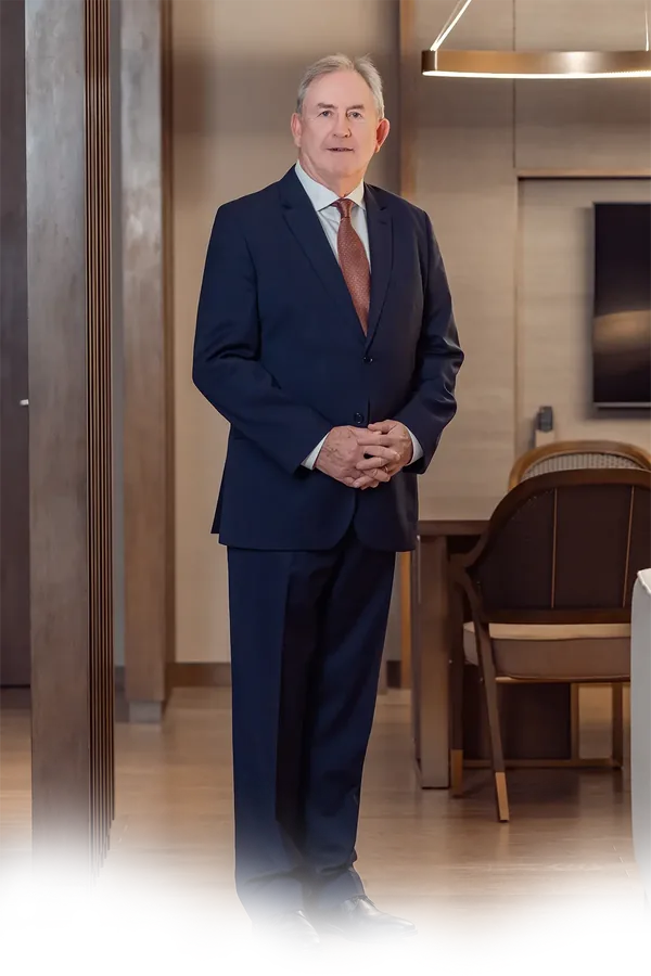 David Thomas standing in a navy suit and tie, hands clasped, in a hotel lounge