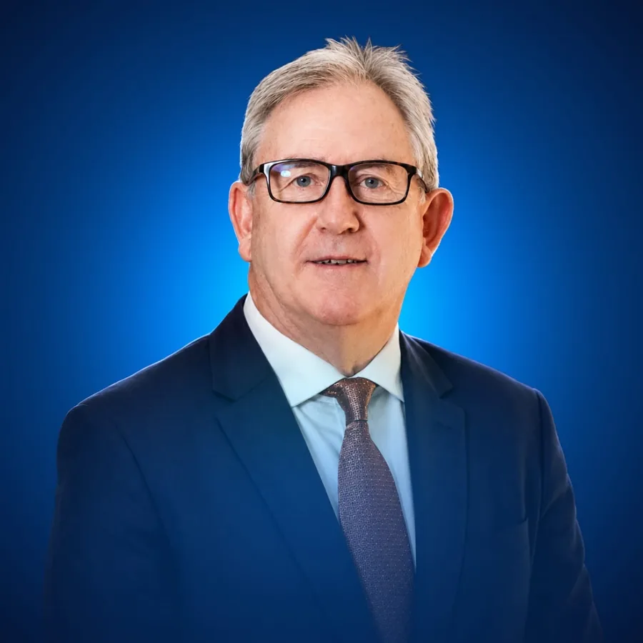 David Thomas, studio headshot in a navy suit and tie against a blue backdrop