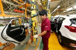 A worker fitting a panel to a white car on a JAC assembly line