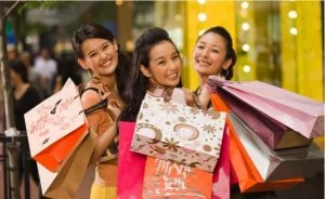 Three young women carrying armfuls of shopping bags through a mall
