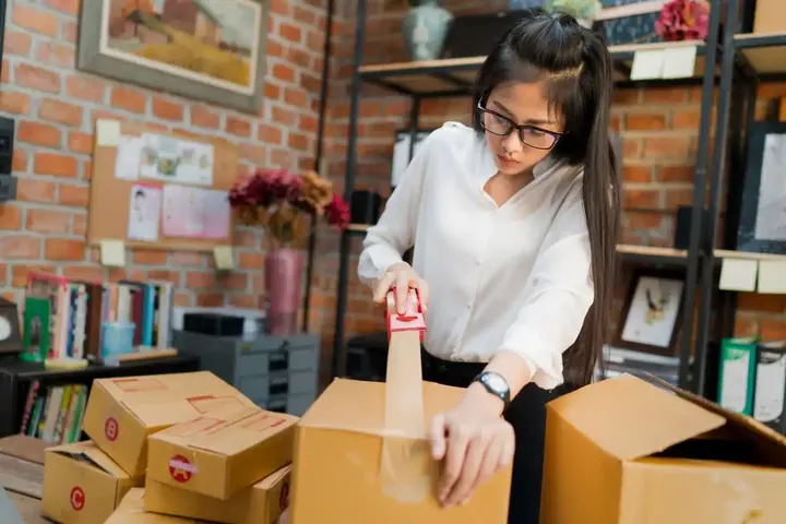 A woman packing cardboard parcels for shipping in a small store