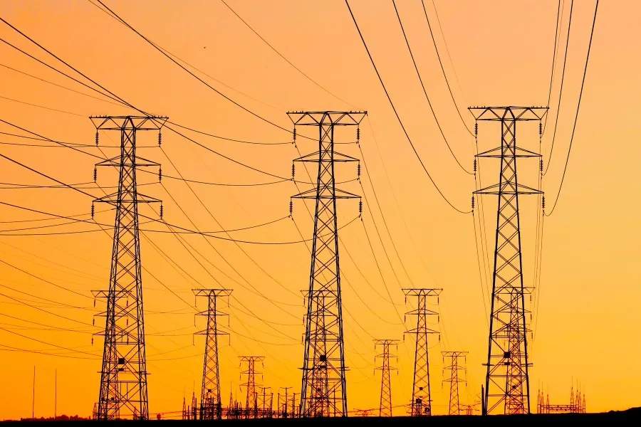 High-voltage transmission towers silhouetted against an orange sunset