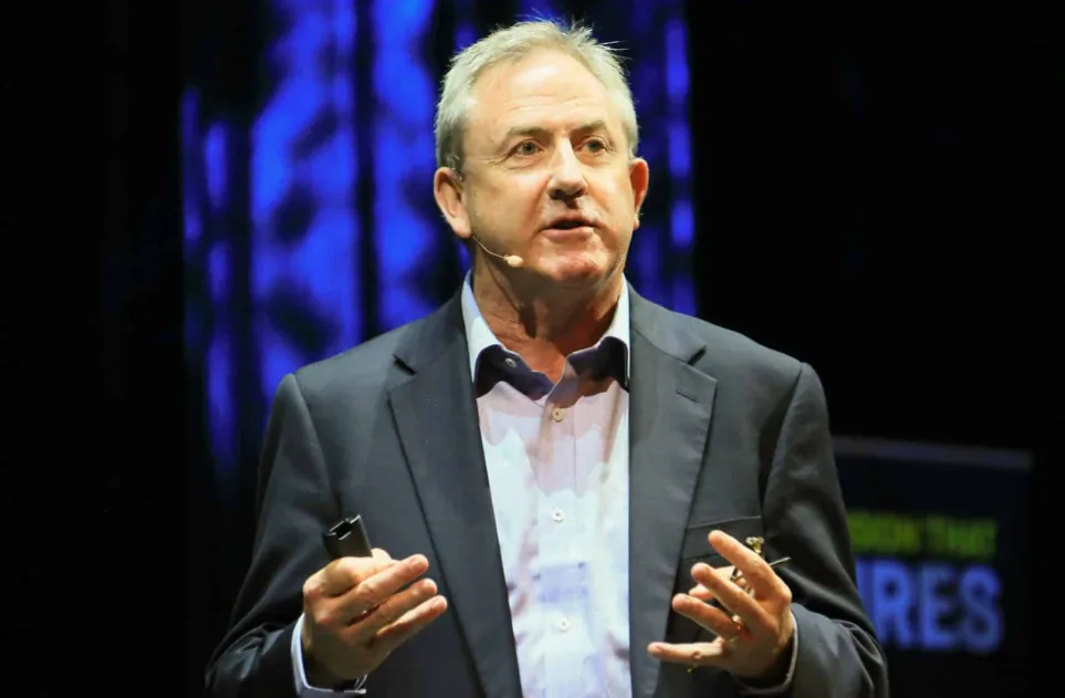 David Thomas speaking into a headset microphone against a blue-lit conference backdrop
